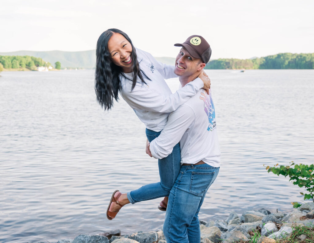 Man picking up woman and smiling in front of a lake