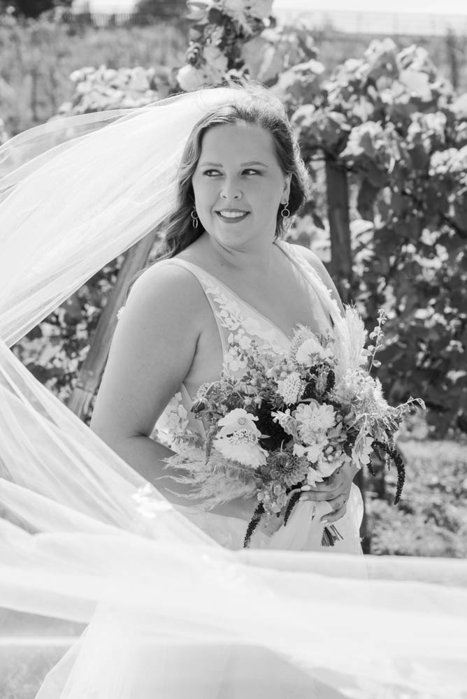 Black and white image of a bride smiling with bouquet with veil draped in front of her towards the camera