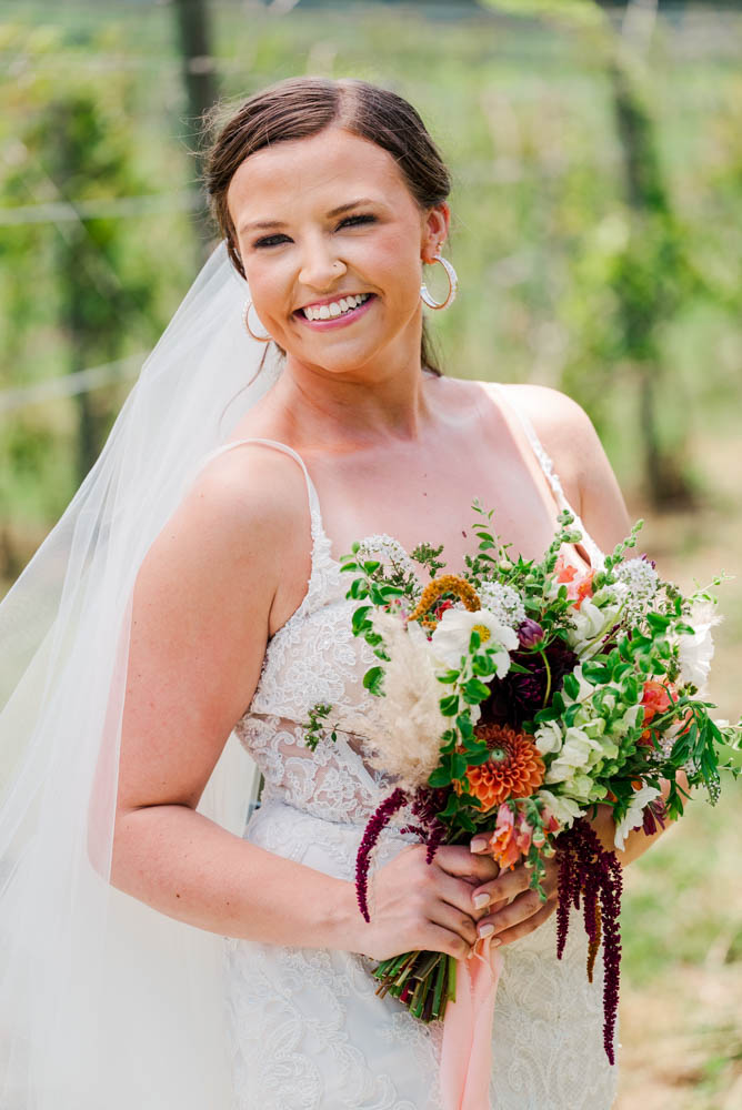 Bride standing in vineyard with her bouquet smiling at the camera